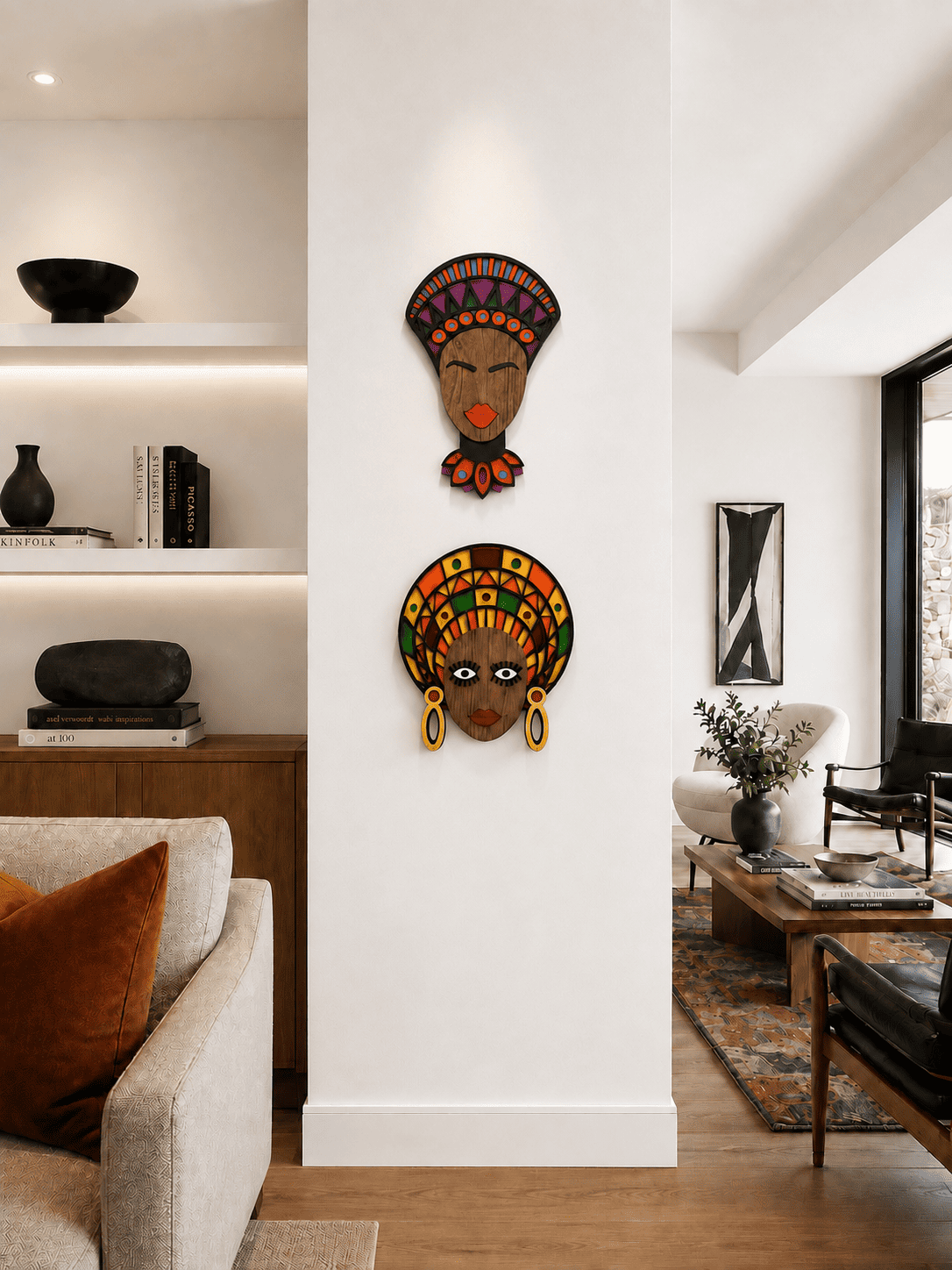 Two colorful African-style wall art masks depicting female heads are displayed on a white pillar in a modern, sunlit living room.
