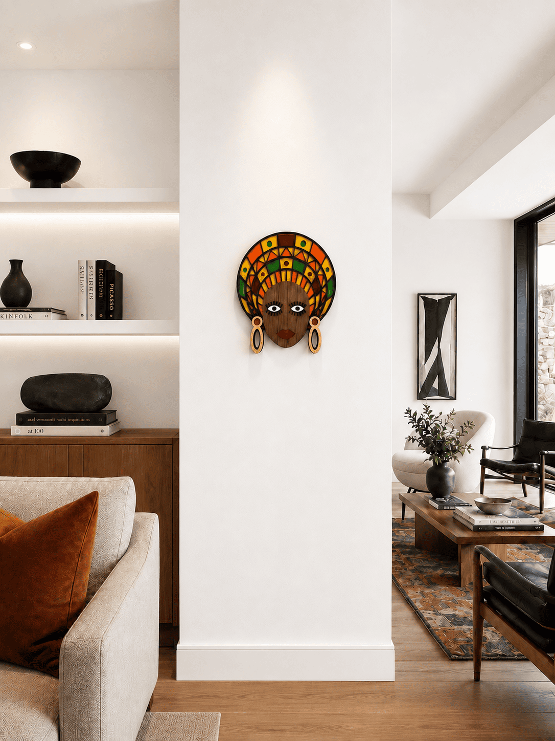 A colorful African-style wall art piece featuring a stylized face with a patterned headwrap and gold hoop earrings, mounted on a white pillar in a modern, sunlit living room - Umasqu