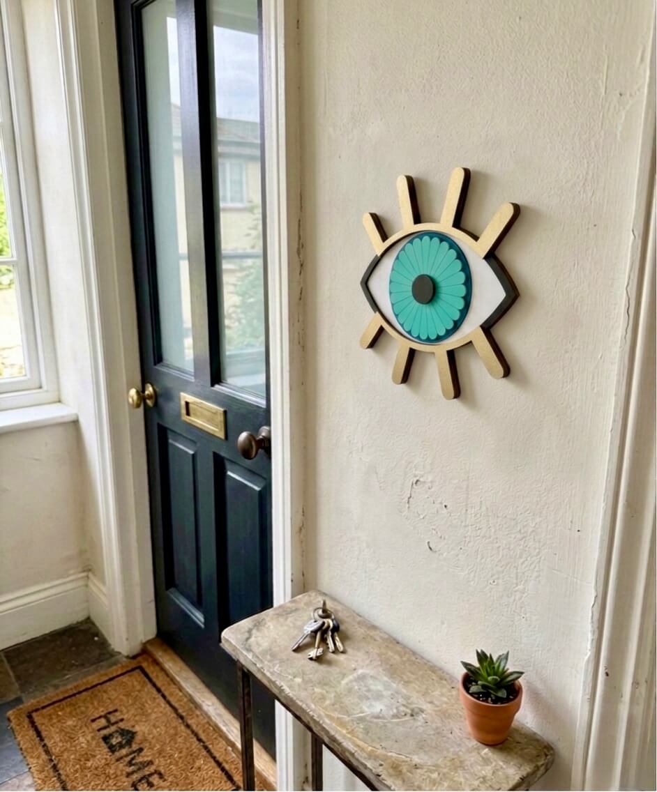 Decorative wall art of an eye on a white wall next to a black door.
