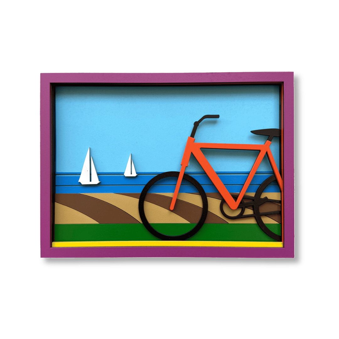 A colorful 3D layered shadow box art print featuring an orange bicycle on a beach with blue water and white sailboats, enclosed in a purple frame - umasqu