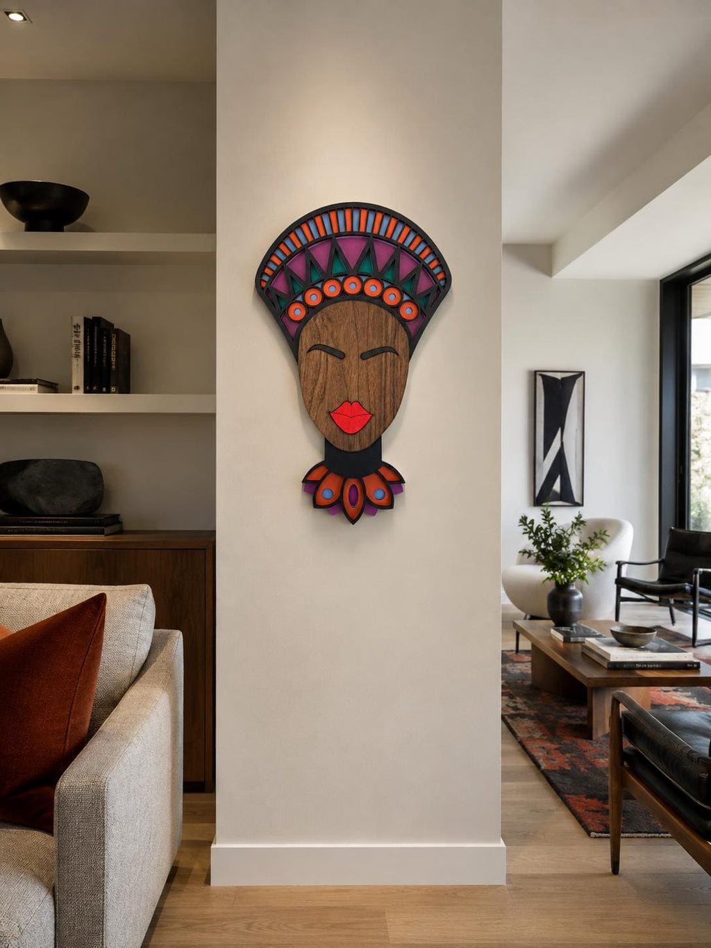 A colorful wooden wall art piece depicting a stylized African face with a patterned headdress, mounted on a white pillar in a modern living room setting. - Umasqu
