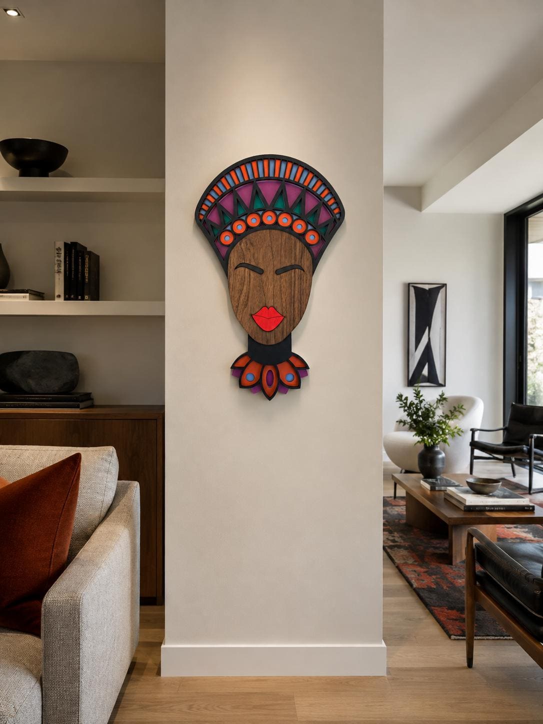 A colorful wooden wall art piece depicting a stylized African face with a patterned headdress, mounted on a white pillar in a modern living room setting. - Umasqu