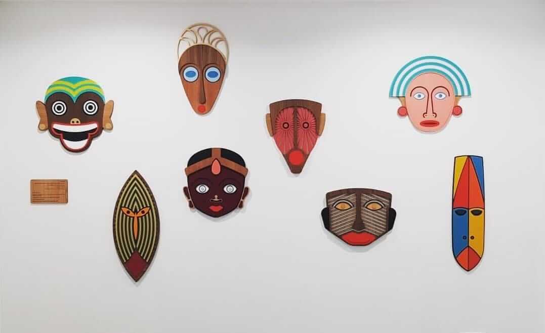 A collection of colorful, hand-carved African wooden masks displayed on a clean white wall.